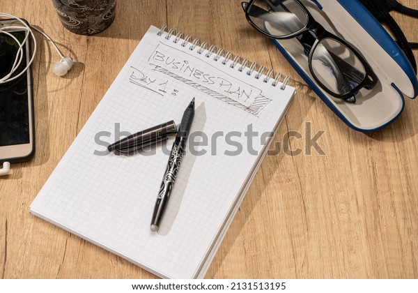 Surface of a wooden desk with a notepad,\
pen, glasses, calculator and cell phone. Job\
desk.