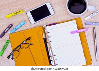 surface of a wooden table with notebook, smartphone, eye glasses, wooden clips with days and pen