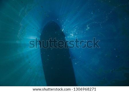 surfboard in beautiful blue water, surfboard image from under water in Clear blue water of lake tekapo in New Zealand, amazing sun in the water with a surfer on it