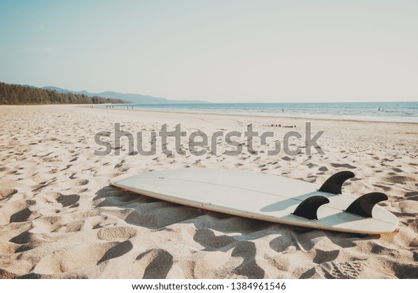 Surfboard on sand tropical beach with\
seascape calm sea and sky background. summer vacation background\
and water sport concept. vintage color tone\
effect.