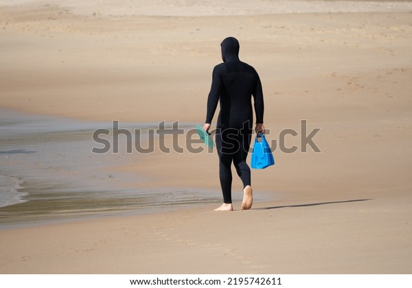 Surfer from behind in black\
wetsuit walking down the sand about to go for a bodysurf at the\
beach