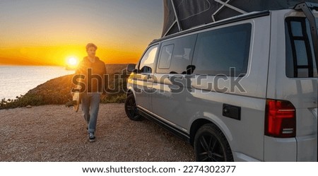 Surfer boy near his mini van and looking on the ocean at summer sunset  with a surfboard on his side