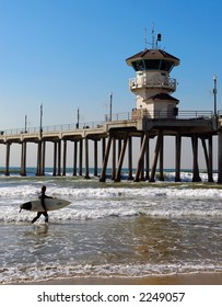 Surfer Carries His Surfboard At Huntington Beach Pier.