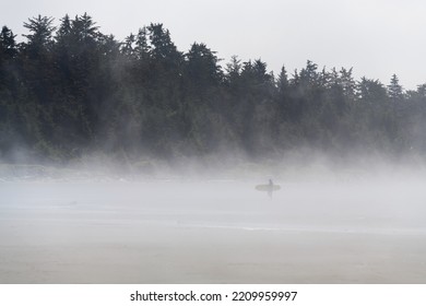 Surfer Carrying Surf Board In The Mist, Chesterman Beach, Tofino, Vancouver Island, Canada.