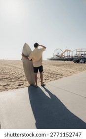 Surfer Casting Long Shadow On Pavement Toward Amusement Pier, Caucasian Male Preparing For Session With Vivid Afternoon Light, Dramatic Silhouette, Distant Ferris Wheel And Empty Sand,