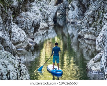 Surfer floating on stand up paddle board on river water in rocky canyon