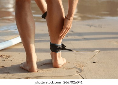 A surfer is getting ready to go into the water with a surfboard. The surfer is wearing a black leash that is attached to the surfboard