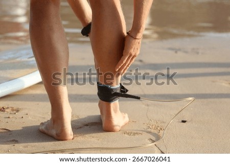 A surfer is getting ready to go into the water with a surfboard. The surfer is wearing a black leash that is attached to the surfboard