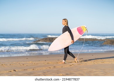 Surfer girl at the beach walking with her surfboard in the morning. Female surfer woman 