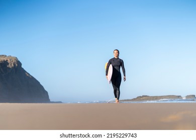 Surfer girl at the beach walking with her surfboard in the morning. Female surfer woman