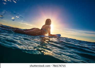 A surfer girl on water surface in sunset sea