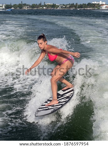 Surfer girl rides wave with fuchsia bright bikini over blue water