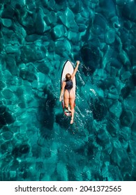 Surfer girl rowing on surfboard in transparent turquoise ocean. Aerial drone view with surfer woman