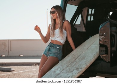 surfer girl sitting at a car with surfboard. california
