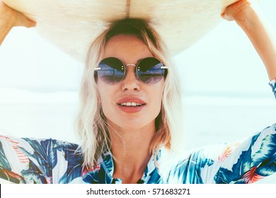 Surfer girl in sport swimwear and sunglasses posing with surfboard on the beach. Active lifestyle and summer vacations.