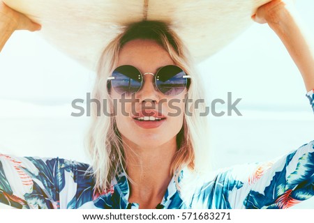 Surfer girl in sport swimwear and sunglasses posing with surfboard on the beach. Active lifestyle and summer vacations.