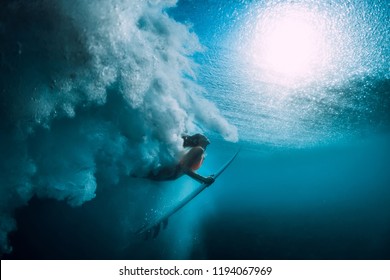 Surfer girl with surfboard dive underwater with under big ocean wave.