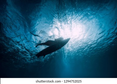 Surfer girl with surfboard dive underwater with under ocean wave.