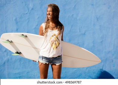 surfer girl with surfboard in front of blue wall - Powered by Shutterstock