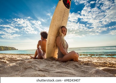 Surfer girls sitting back to back with surfboard in between in front of a breathtaking seascape on summer day, watching waves at beautiful Padang Padang beach, Bali, Indonesia - Powered by Shutterstock