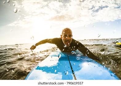 Surfer guy paddling with surfboard at sunset in Tenerife with unrecognizable people at surf boards on background - Sport travel concept with shallow depth of field with drops on lens as composition