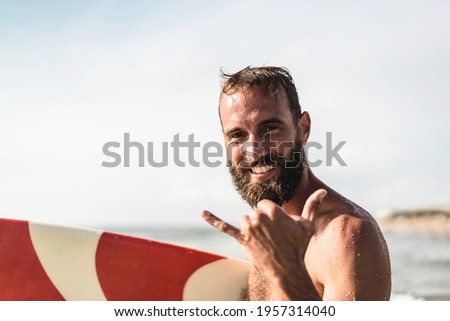 Surfer happy with surf surfing smiling doing hawaiian shaka hand sign for fun during surf session in ocean waves on beach vacation -  Surfing travel destination - Friendly greeting in surfer culture