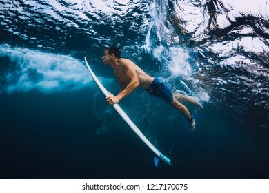 Surfer man with surfboard dive underwater with ocean wave.