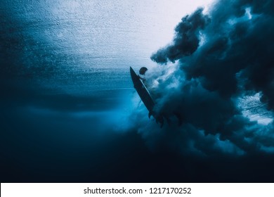 Surfer man with surfboard dive underwater with under ocean wave.