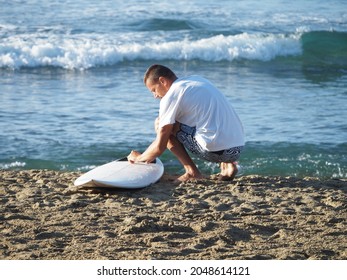 Surfer Man Wearing Boardshorts On Surf Beach, Waxing White Surfboard.