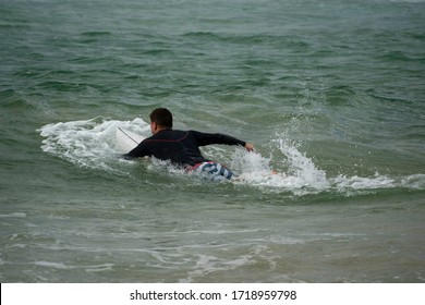 Surfer On His Surfboard Paddling Away Viewed From Behind, Paddling Out To Catch Some Waves