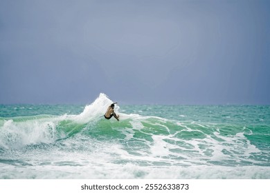 A surfer on a shortboard carves an aggressive top turn (smacking the lip) on a frothy green and white ocean wave with a thick gray blue stormy sky in the background; concept: fly, action, surf - Powered by Shutterstock