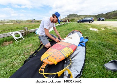 Surfer on vacation waxing surf board outdoors on the beach. Man is removing or applying wax to surfboard shortboard on vacation. Traces of wax are visible. Atlantic Ocena - Spain. - Powered by Shutterstock