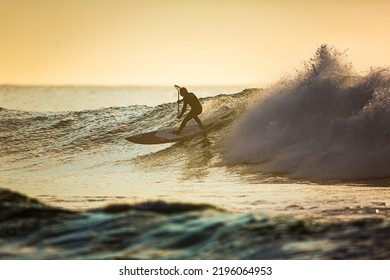 A Surfer With A Paddle Rides On The Crest Of A Large Wave With Foam At Dawn. Surfing Man. Extreme Water Sport Concept. Stand Up Paddle Board - 14 JUL 2015 Vladivostok Russia