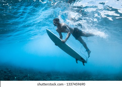 Surfer performs dive (the duck dive) with his surfboard under the wave