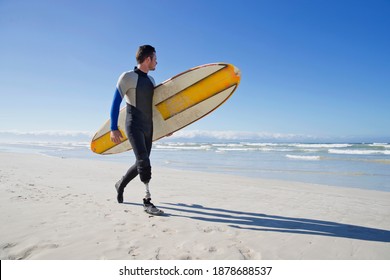 Surfer With a prosthetic Leg Walking On the Beach carrying a surf board - Powered by Shutterstock