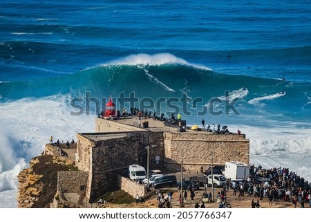 Surfer riding huge wave near the Fort of Sao Miguel Arcanjo Lighthouse in Nazare, Portugal. Nazare is famously known for having the biggest waves in the world.