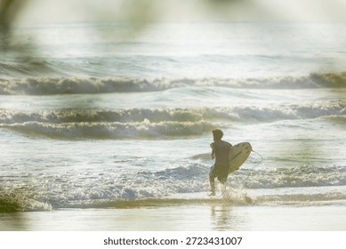 Surfer running into the ocean waves with surfboard at sunset in Costa Rica
