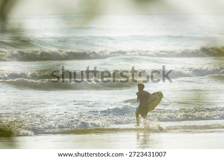 Surfer running into the ocean waves with surfboard at sunset in Costa Rica