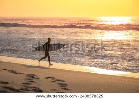 Surfer running on the beach with the waves at sunset in Portugal.