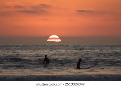 Surfer silhouettes sitting on surfboards in ocean waves watching orange pink sunset in Pacific Beach, San Diego - Powered by Shutterstock