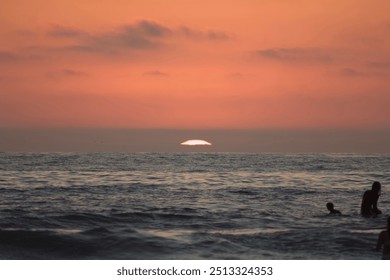 Surfer silhouettes sitting on surfboards in ocean waves watching orange pink sunset in Pacific Beach, San Diego - Powered by Shutterstock