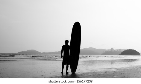 Surfer standing on the beach, close to the sea, contemplating the waves