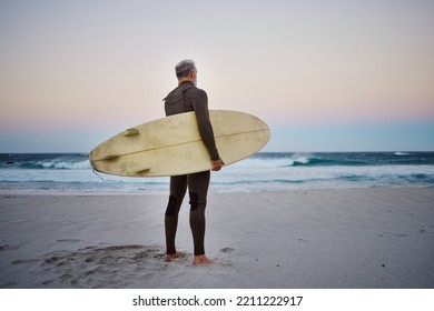 Surfer, surfboard and senior man on beach at sea waves in during sunset during summer vacation in Hawaii. Professional male athlete rest after training or practice surfing sport outdoor at the ocean - Powered by Shutterstock