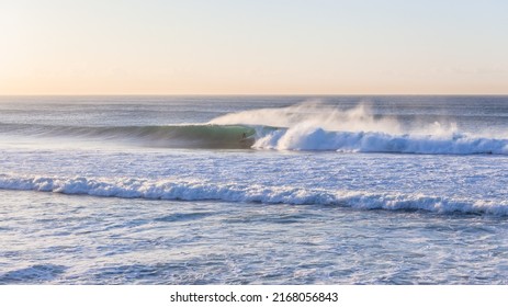 Surfer surfing tube rides good size  ocean wave morning telephoto land photo .