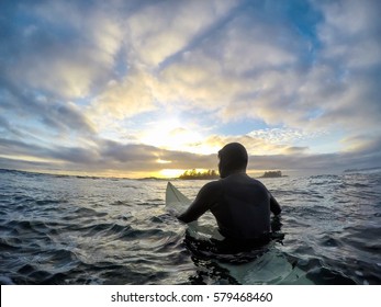 Surfer waiting for the waves at the ocean in Tofino, Vancouver Island, British Columbia (BC), Canada, during a colorful winter sunset.