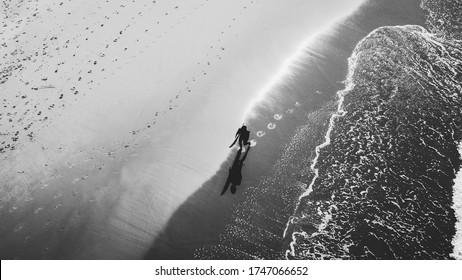 A surfer walking down the beach after a surf. Shot in black and white. - Powered by Shutterstock