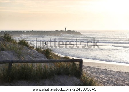 A surfer walking on the beach at dawn.