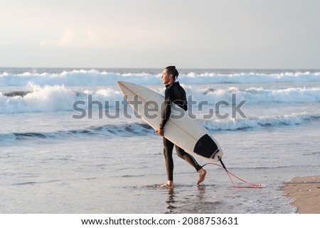 surfer walking on the beach smiling with a surfboard getting into the ocean	