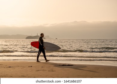 Surfer walking with surfboard on the seashore beach at sunset or sunrise. Silhouette of surf man looking for the high waves. Outdoors water sports, vacation and adventure lifestyle concept. - Powered by Shutterstock