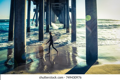 Surfer walking under Huntington beach pier in southern California, vintage effect sunlight flare